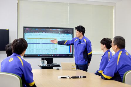 モニターの前に集まり、スライド資料を見ながら研修を受けているスタッフたちの様子